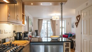 A modern kitchen with stainless steel appliances, a central island, and a dining area with a sofa. - Beautiful Two BD Home Near Cirencester (Stratton)