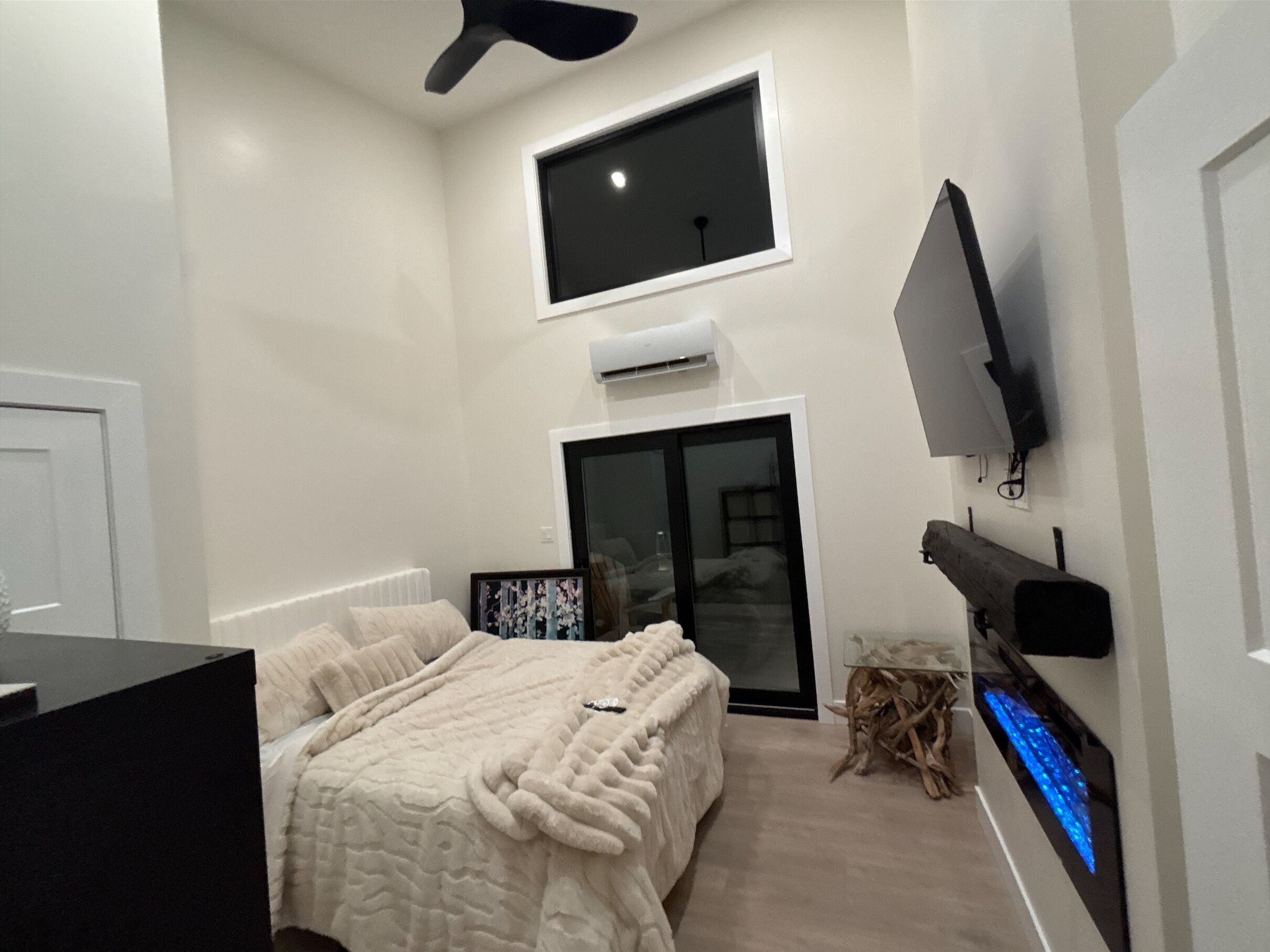 Une chambre à coucher avec un lit, un téléviseur fixé au mur, un ventilateur de plafond et une fenêtre.