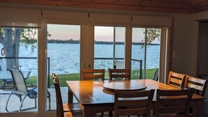 A wooden table and chairs inside a room with large glass doors leading to a lakeside view. - Sunset spectacular with resort amenities (Kawartha Lakes)