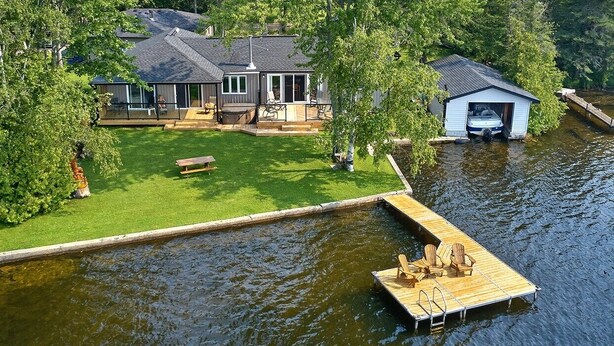 A lakeside house with a dock, a covered boat launch, and a well-maintained lawn. - Sunset spectacular with resort amenities (Kawartha Lakes)