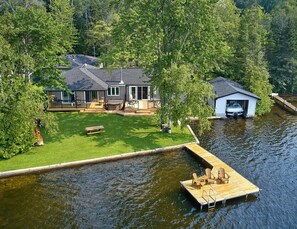 Ein Haus am Seeufer mit Anlegesteg, überdachter Bootsrampe und gepflegtem Rasen.