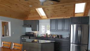 A modern kitchen with a central island, dark cabinets, stainless steel appliances, and a wooden ceiling. - Sunset spectacular with resort amenities (Kawartha Lakes)