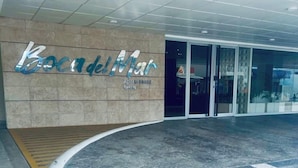 Entrada de un hotel de diseño moderno, con una rampa curva que conduce a la entrada, un letrero grande con el nombre del hotel y una puerta de cristal.