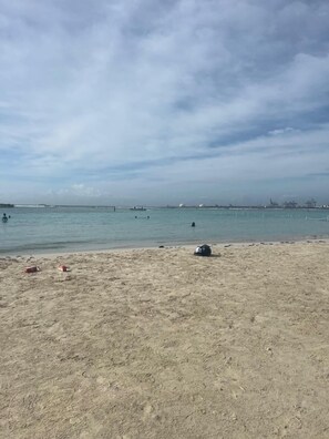 Una playa con arena, agua y construcciones a lo lejos.