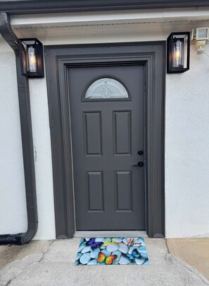 Puerta gris oscura con un panel de vidrio decorativo y felpudo con mariposas.