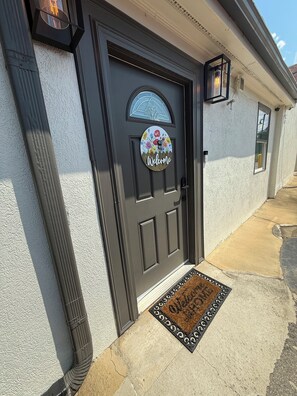 A dark grey door with a welcome sign, a window with a decorative grill, and a doormat. - Cozy 2-bedroom house in lovely Marietta with AC (MARIETTA)