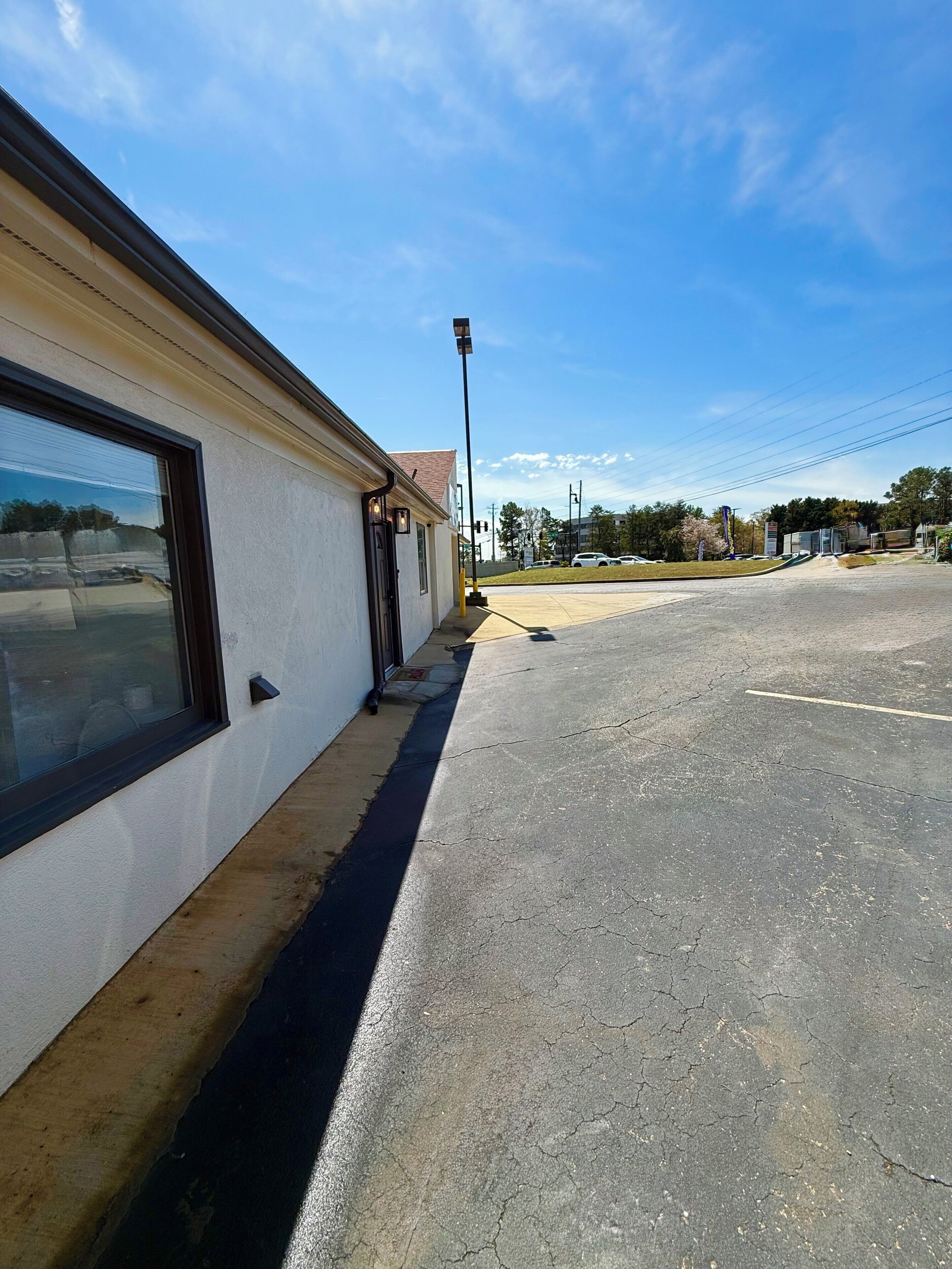 A building with a large window, a sidewalk, and a parking lot.