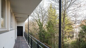 A corridor with a black door, a brick floor, and a railing overlooking a forested area. - Plac Wilsona Charming Apartment (Warszawa)