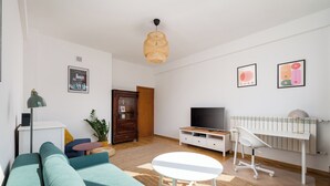 A living room with a sofa, TV, white desk, and a hanging light fixture. - Plac Wilsona Charming Apartment (Warszawa)