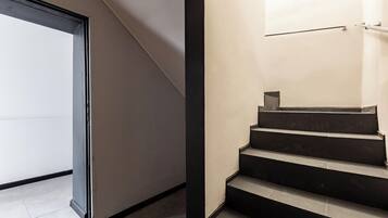 Un escalier moderne au design minimaliste, une porte en verre à gauche et une main courante en métal à droite.