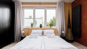 A double bed with white linens, a dark wardrobe, a radiator, and a window with curtains.