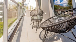 En balkon med et glasbord og stole, en fletstol og udsigt over det omkringliggende område.