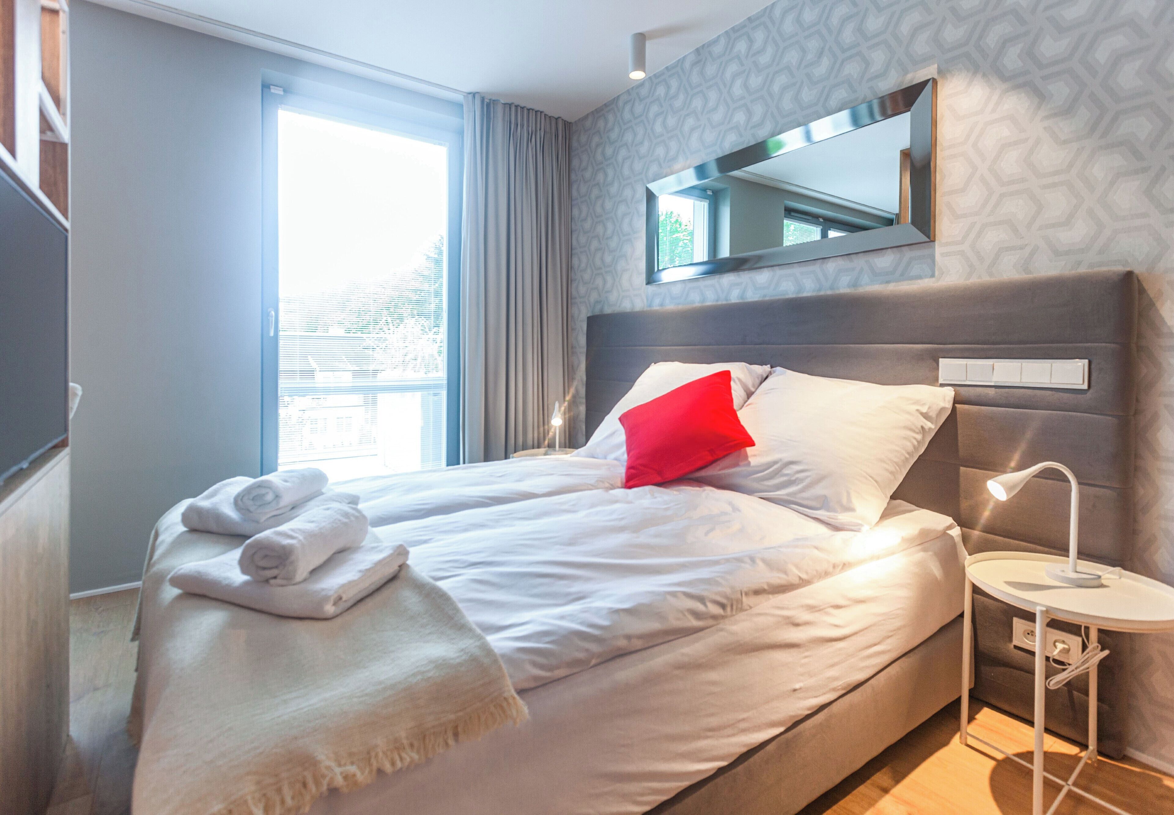 A neatly made bed with towels, a red pillow, and a bedside table with a lamp.