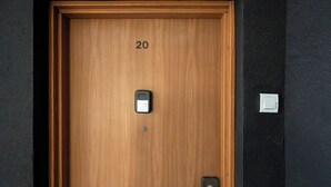 Une porte en bois avec le numéro « 20 » au-dessus, un interphone et une poignée de porte.