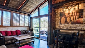 Um quarto espaçoso com uma janela grande, um sofá de couro, uma mesa de jantar e um display de barris de vinho fixado na parede.