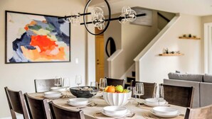 Una zona de menjador amb una taula preparada per a sis persones, un plat de fruita i una làmpada de cristall moderna.