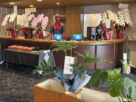 Un mostrador de recepción con orquídeas, una figura de Spider-Man y una pantalla digital.