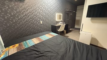 Una habitación con cama, escritorio, silla, espejo, armario y televisor.