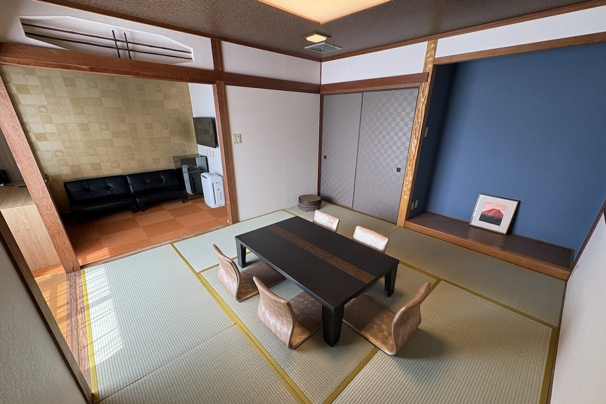 A traditional Japanese-style room with tatami flooring, a low table with cushions, a black sofa, and a blue accent wall.