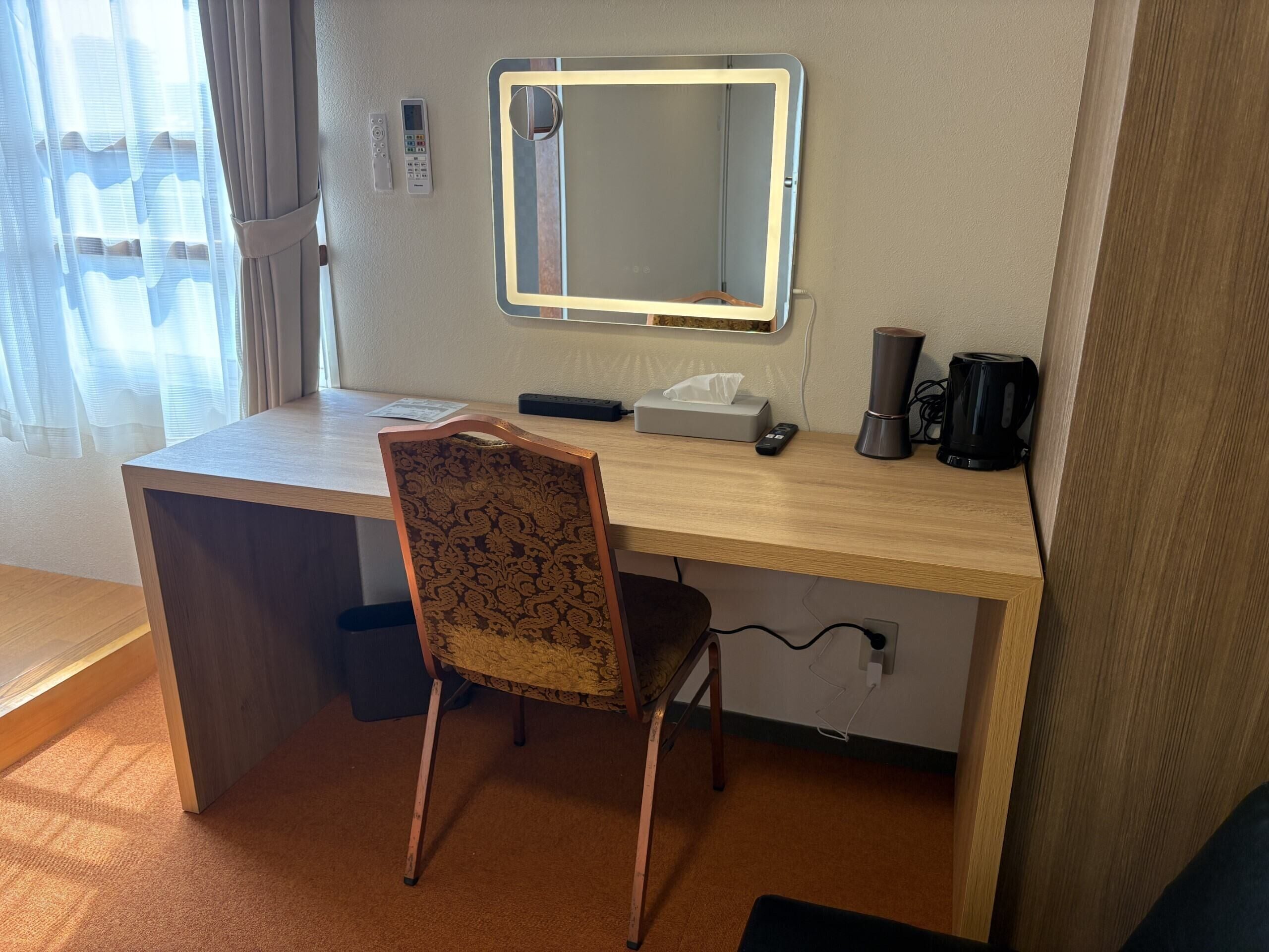 Habitación de hotel con un escritorio de madera, una silla, un espejo, una cafetera y una caja de pañuelos.