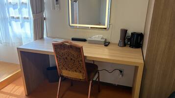 Habitación de hotel con un escritorio de madera, una silla, un espejo, una cafetera y una caja de pañuelos.