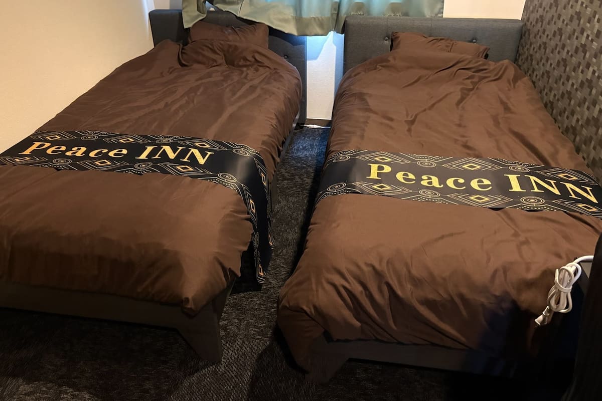 Twin beds with 'Peace INN' branding, a grey headboard, and a patterned wall.
