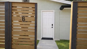 A gated entrance with a wooden fence, a white door, and a concrete path leading to a building. - Quiet Downtown Clermont Stay Near Waterfront Park (Clermont)
