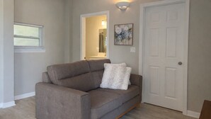 A neutral-toned living room with a gray sofa, a white door, and a painting on the wall. - Quiet Downtown Clermont Stay Near Waterfront Park (Clermont)