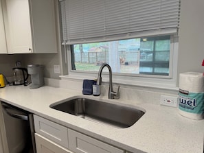 A kitchen with a stainless steel sink, a coffee maker, and a toilet paper dispenser.