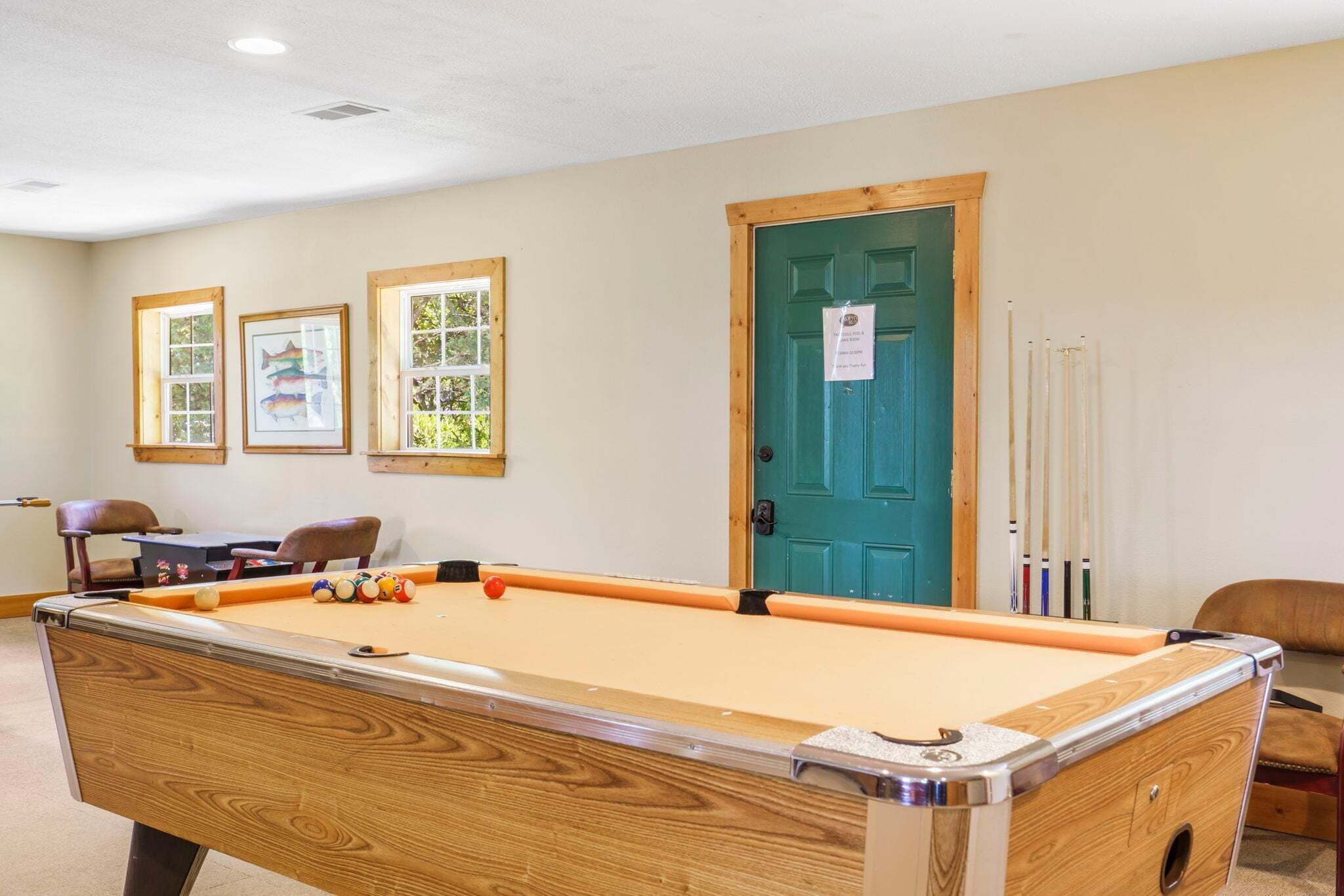 A pool table with balls, a door, and two framed pictures on the wall.