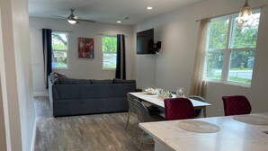 A modern kitchen with a dining area, a gray sofa, and a ceiling fan. - The Oasis on Waters -New Home (Tampa)