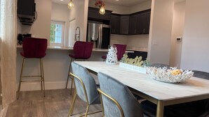 A modern kitchen with a marble countertop, two bar stools, pendant lighting, and a dining table with chairs. - The Oasis on Waters -New Home (Tampa)