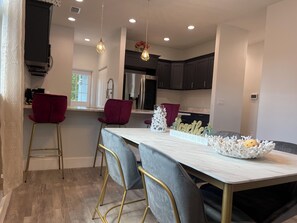 A modern kitchen with a marble countertop, two bar stools, pendant lighting, and a dining table with chairs. - The Oasis on Waters -New Home (Tampa)