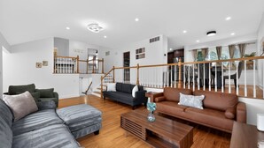 A spacious living area with a staircase, multiple seating options, and a wooden floor.