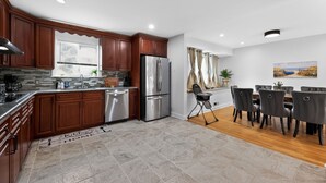 A modern kitchen with wooden cabinets, a stainless steel refrigerator, and a dining area with a table and chairs.