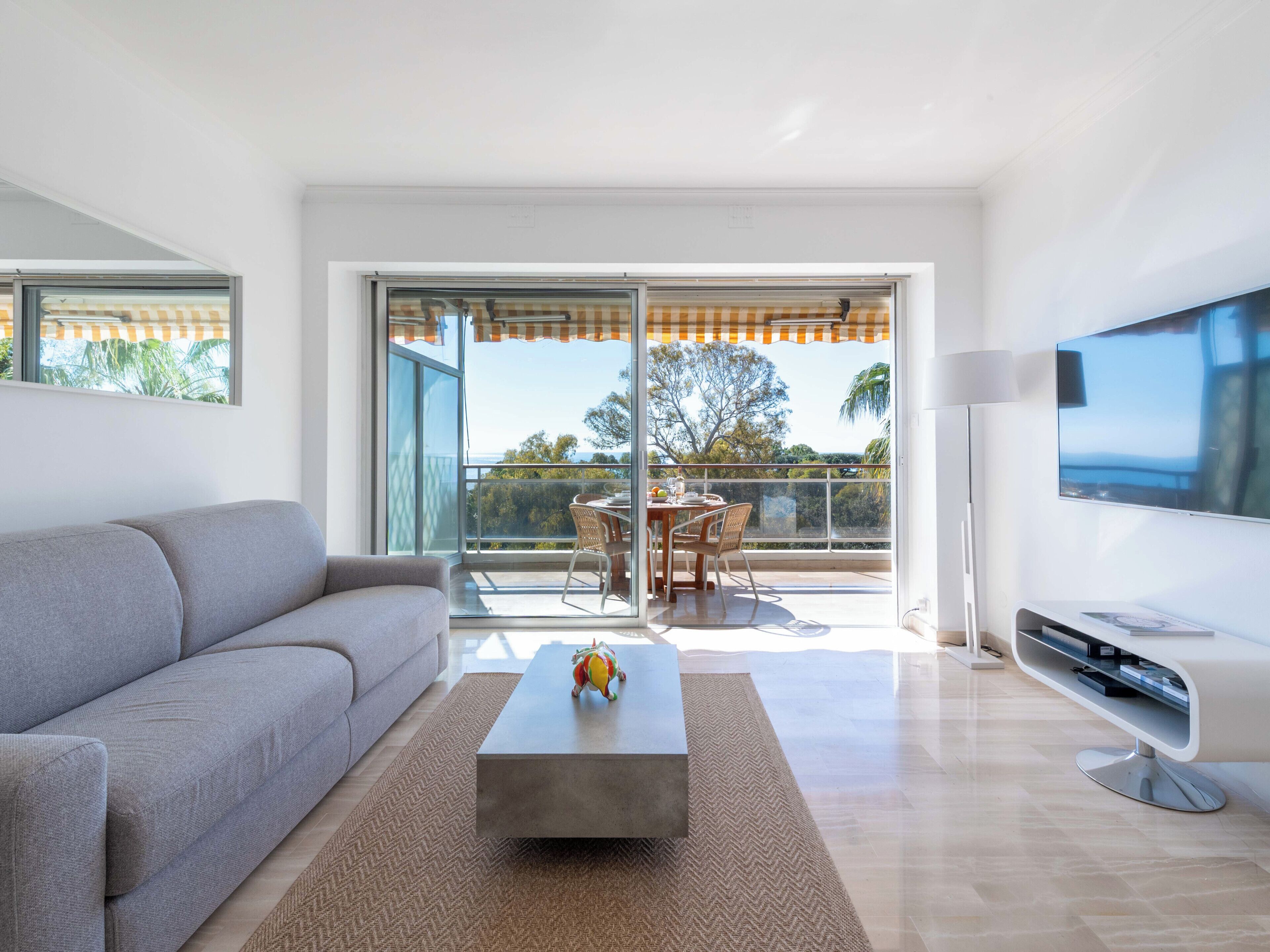 Una sala de estar moderna con sofá, mesa de centro, televisión y un balcón con mesa y sillas.