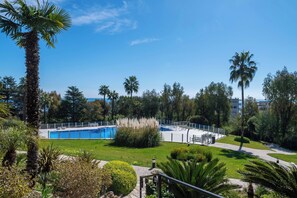 A pool area with palm trees, a clear sky, and a pathway. - 1-Br Sea-View Apartment – Prestigious Residence – Parking (Vallauris)