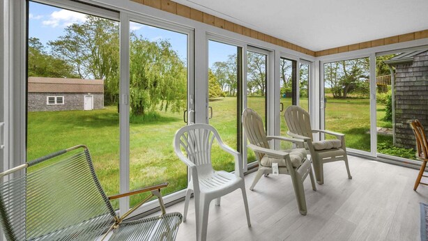 Una habitación soleada con ventanas amplias, techo de madera y vista a un jardín césped.