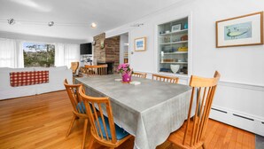 Un comedor con chimenea de ladrillo, sillas de madera, una mesa con mantel gris y vistas al exterior.