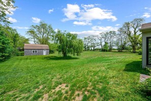 A grassy yard with a small wooden shed and a house with a sloped roof. - Relaxing Barnstable Getaway Close to the Beach (Barnstable)