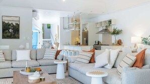 Ein modernes Wohnzimmer mit einer Sofagarnitur, einem Couchtisch und einer im Hintergrund sichtbaren Küchenzeile.