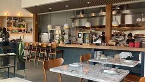 A restaurant interior with marble tables, wooden chairs, a bar area with bottles, and a kitchen in the background. - Green Lake's 2B Lower Unit with Parking (Seattle)