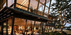 A modern building with large glass windows, a dining area with tables and chairs, and a view of trees. - Green Lake's 2B Lower Unit with Parking (Seattle)