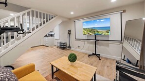 A modern room with a staircase, a projector screen, a treadmill, and a small table with a plant. - Green Lake's 2B Lower Unit with Parking (Seattle)