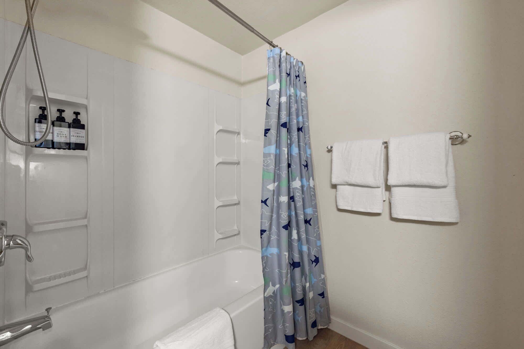 A bathroom with a shower, a towel rack with towels, and a shelf with toiletries.