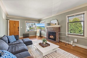A living room with a fireplace, a sofa, a coffee table, and a view of a beach through the windows. - 4B Pet-friendly Home by Green Lake (Seattle)