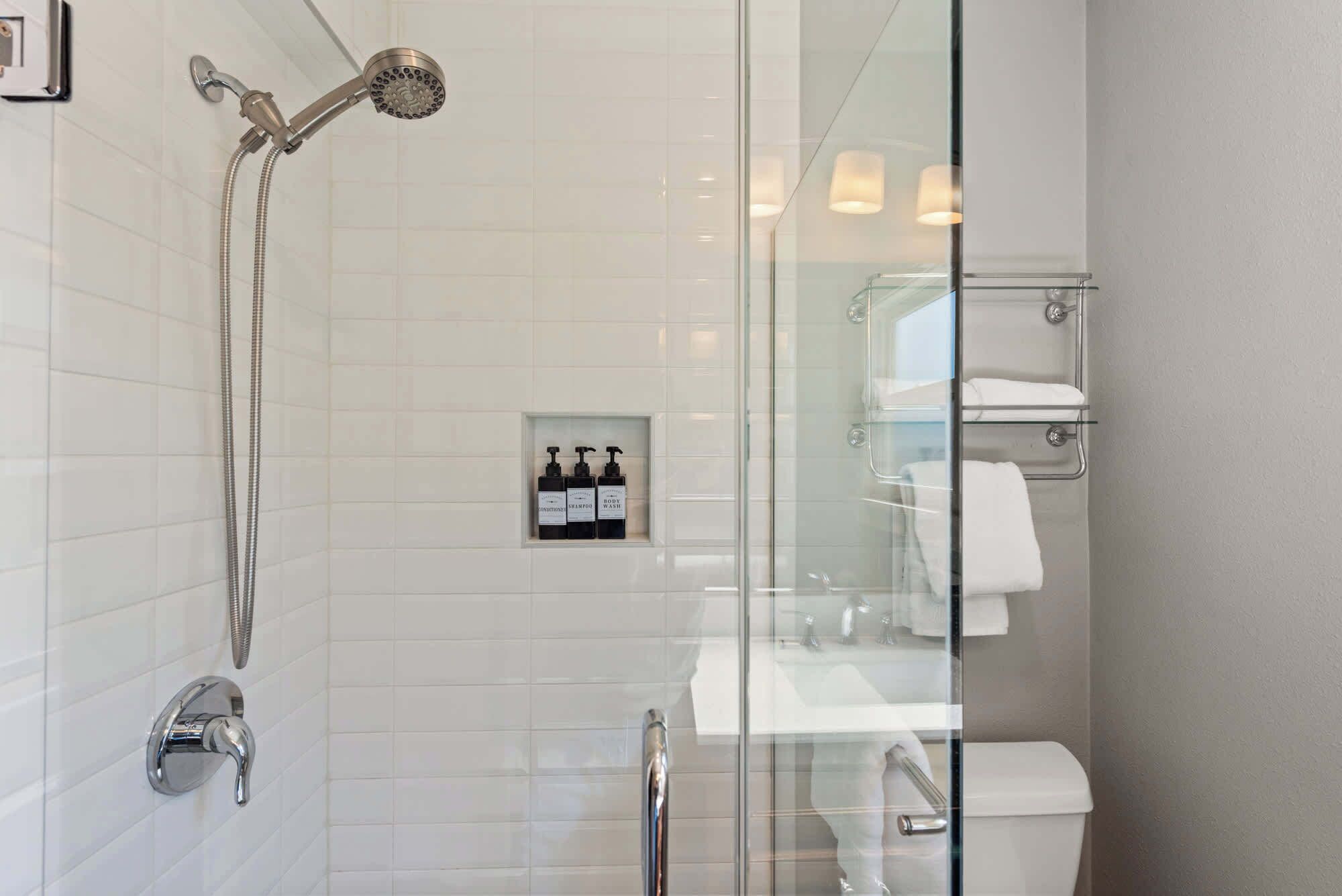 Un baño moderno con cabina de ducha de vidrio, pared con azulejos blancos y separador de vidrio que divide la ducha del área del inodoro.