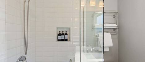 Un baño moderno con cabina de ducha de vidrio, pared con azulejos blancos y separador de vidrio que divide la ducha del área del inodoro.