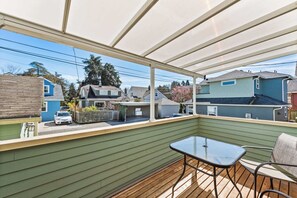 Une terrasse couverte, avec une table et des chaises, donnant sur une rue résidentielle.