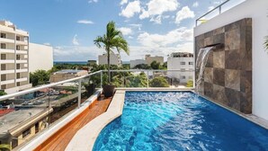 A rooftop pool with a waterfall feature, surrounded by a glass railing, and overlooking a cityscape. - Bleu Balam • Quiet • Pool • Zazil-Ha • 1 Block to 5th Ave (Playa del Carmen)